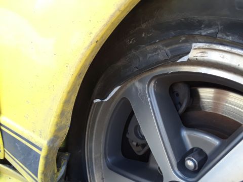 2003 Ford Mustang - Close-up of a damaged tire and rim on a yellow vehicle, showing the fender and part of the wheel.