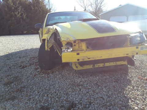 2003 Ford Mustang - This yellow car has significant damage to its front end, including the bumper and fender.