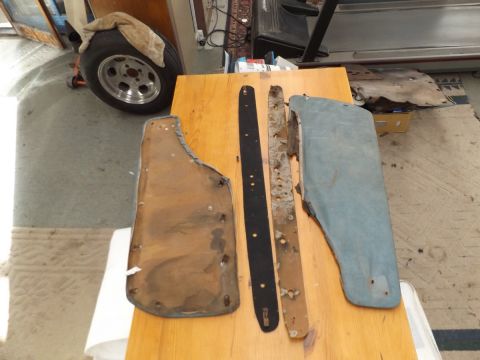 1962 MG B - Several car parts, including mud flaps and trim pieces, are displayed on a table with a spare tire in the background.