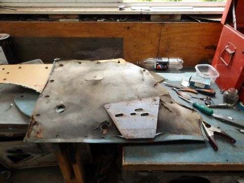 1962 MG B - A weathered car door panel lies on a workbench, surrounded by tools and a plastic bottle.