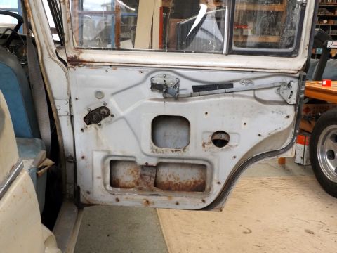1962 MG B - The interior of a car door reveals rust and mechanical components, with a partial view of the seats and steering wheel.