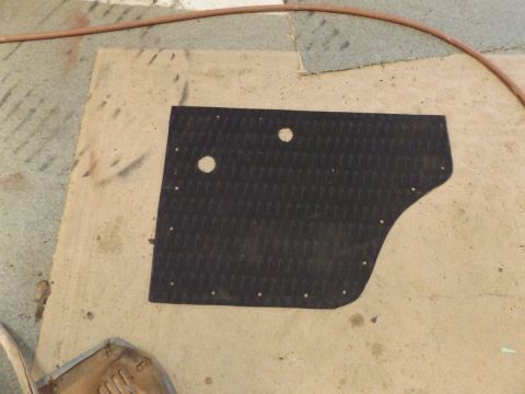 1962 MG B - A black rubber floor mat, likely for a vehicle interior, is shown on a tan surface. The mat has two circular cutouts and numerous small hol…