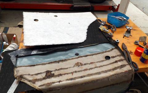 1962 MG B - Disassembled car door panel and associated hardware parts are on a workbench for repair or restoration.