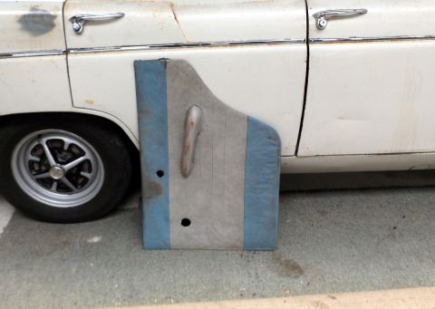 1962 MG B - A detached car door panel with a chrome handle is shown next to a white vehicle.
