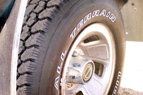 1995 Ford Bronco - Close-up of a raised-white-letter 'ALL TERRAIN' tire mounted on a polished five-slot alloy wheel with a small center cap, shot low from the…