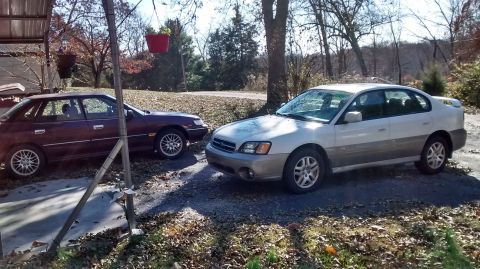 1994 Subaru Legacy - Two Subaru sedans are parked in a driveway on a sunny day with trees in the background.