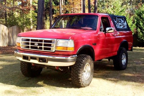 1994 Ford Bronco - This red Ford Bronco SUV is shown from a three-quarter front view, parked outdoors on a grassy area.