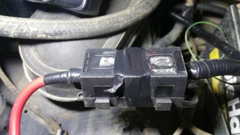 1996 Ford Bronco - A close-up shot shows a black plastic fuse box with a red wire and black electrical tape, likely part of a vehicle's electrical system.