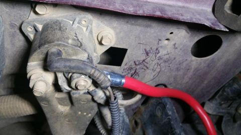 1996 Ford Bronco - Detail of automotive wiring, likely for an alternator upgrade, showing a red cable connected to a mechanical part.