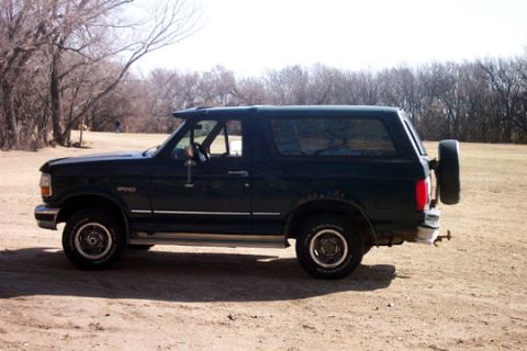 1995 Ford Bronco - Side profile of a dark green 1995 Ford Bronco, a spare tire mounted externally on the rear.