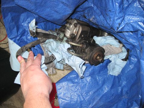 1994 Cadillac Fleetwood - A hand reaches for a steering gear box covered by a blue tarp and shop towels.