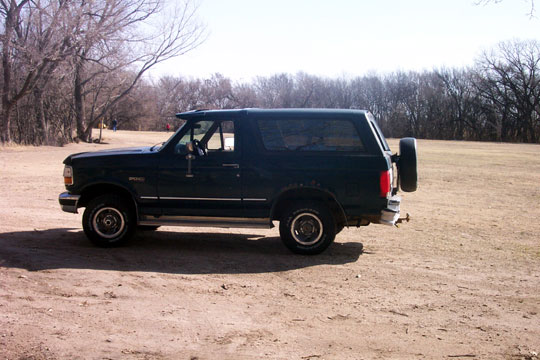 1995 Ford Bronco, side view, parked on dirt lot with bare trees
