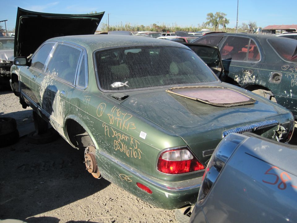 Green Jaguar XJ sedan with hood open, missing wheels, and handwritten text on the trunk