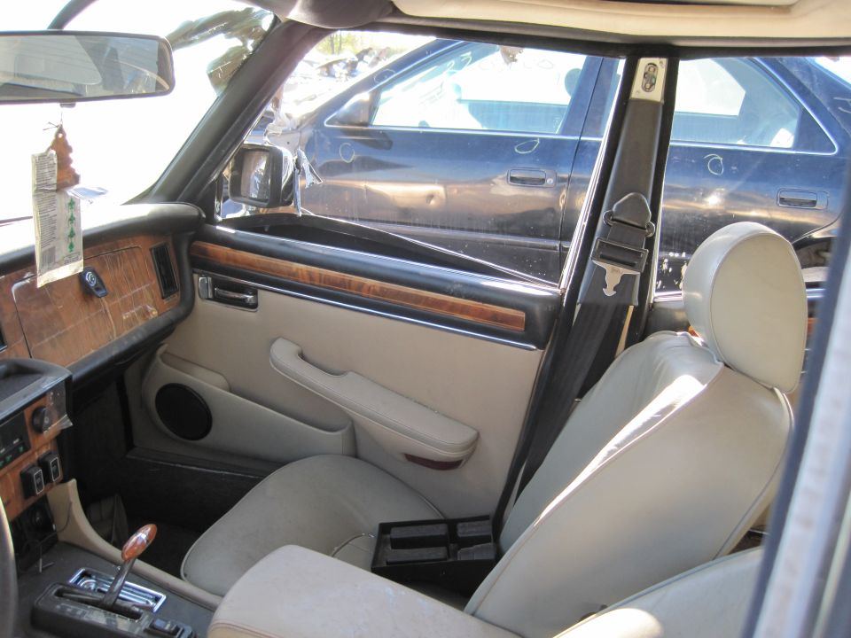 Interior of a 1985 Jaguar XJ6, showing tan seats, wood trim dashboard, and a black car visible through the window