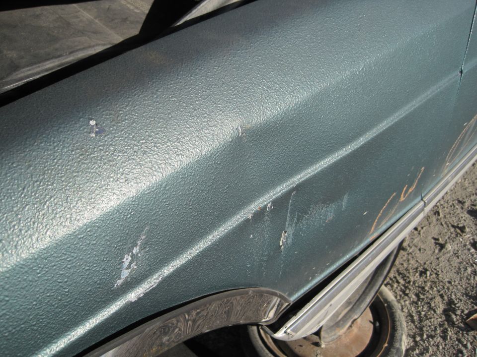 Teal car fender with textured paint, scratches, and a dent near the wheel well