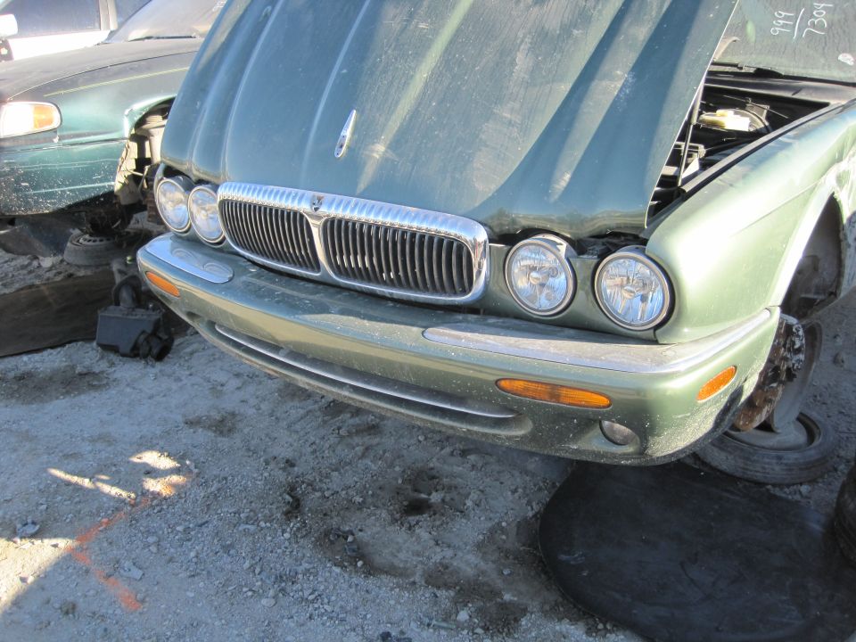 Green 1985 Jaguar XJ6 front end with hood open, parked in a junkyard