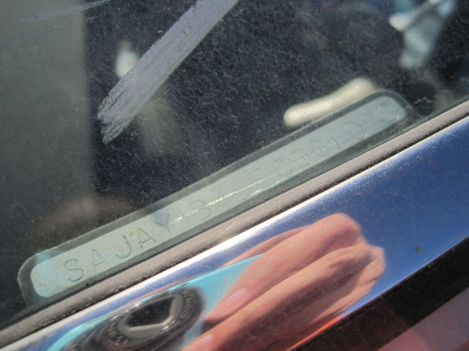 Close-up of a VIN plate on a 1985 Jaguar XJ6 windshield, showing 'SAJAY13' and other characters