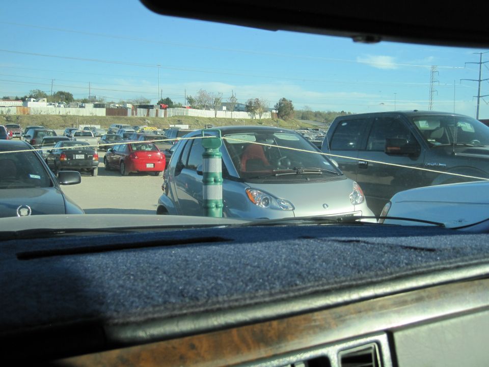 Silver Smart Fortwo parked in a lot with other cars. Green and white striped pole in front
