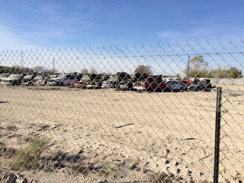 Many cars parked in a junkyard under a clear blue sky