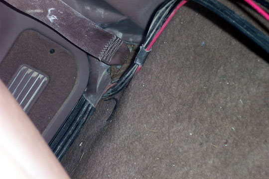 Driver footwell with brown carpet, dead pedal, and routed black and pink wiring