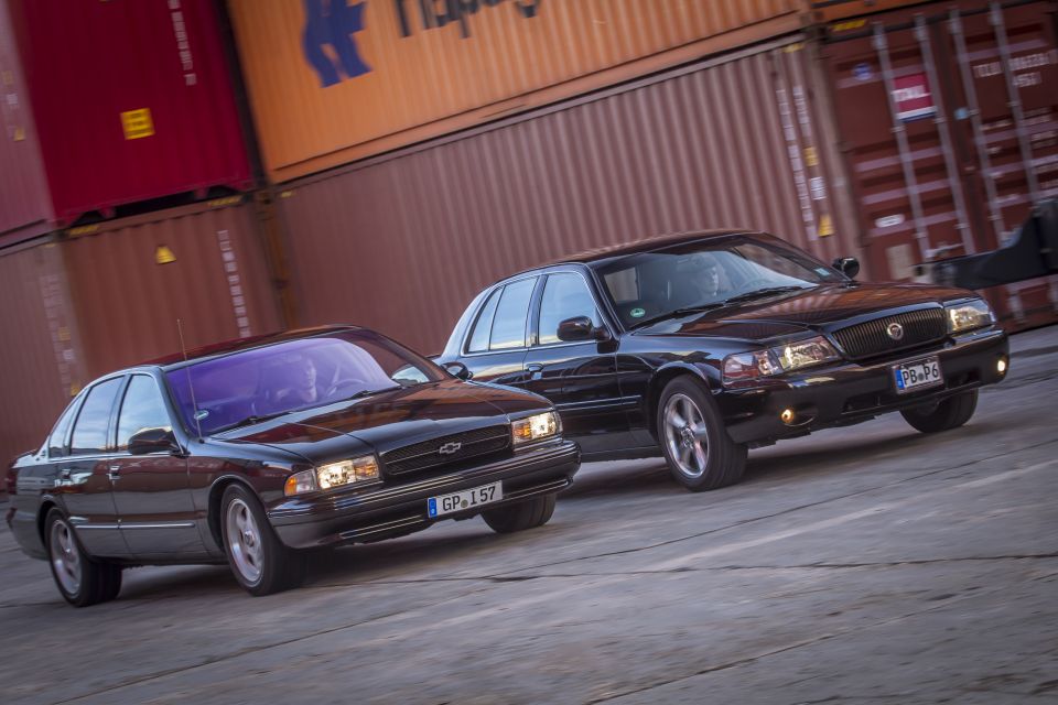 Two black sedans, a 2003 Mercury Marauder and a Chevrolet Impala, drive past shipping containers