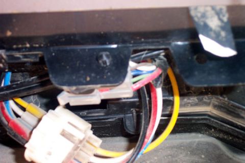1995 Ford Bronco - Close-up of automotive wiring behind a black plastic trim panel, showing white multi-pin connectors and a bundle of red, yellow, blue, gree…