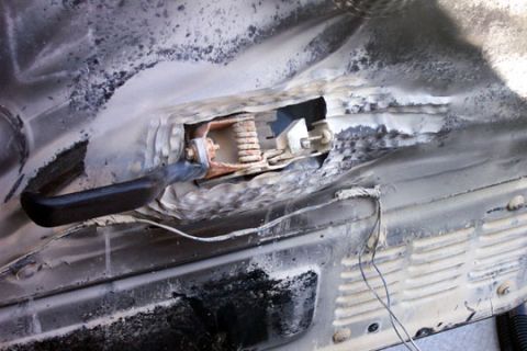 1995 Ford Bronco - Close-up of a rusted-through and burned area of body sheet metal around a door or fender opening, with flaking paint, charred black residue…