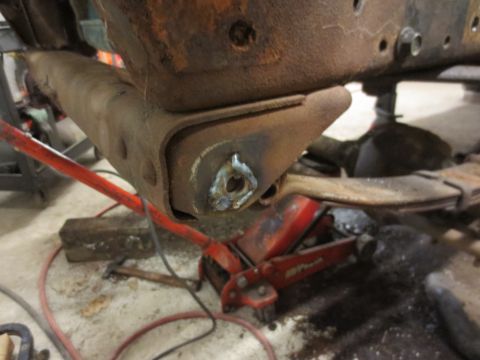 1967 Ford F-250 - Close-up of a heavily rusted truck frame section, supported by a red hydraulic jack, with evidence of recent welding.