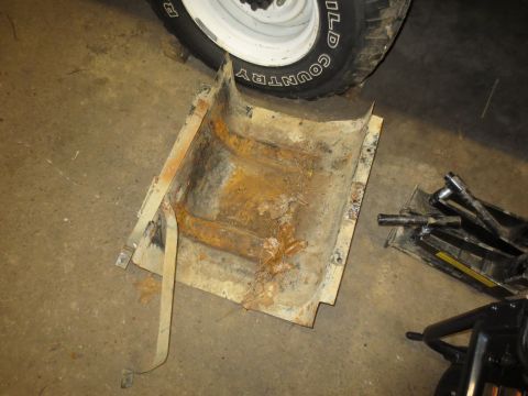 1967 Ford F-250 - A rusty truck part, possibly a fuel tank skid plate, lies on a concrete floor next to a tire.