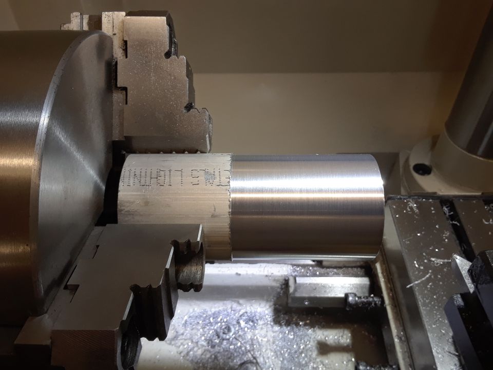 Metal cylinder being machined on a lathe, with text 'ETMS LIGHTNING' visible