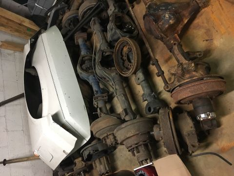1967 Ford F-250 - A collection of vehicle axle assemblies and a white fender are stored indoors.