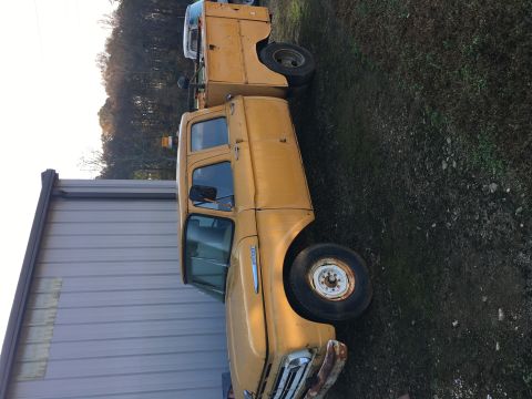 1967 Ford F-250 - A yellow 1967 Ford F-250 truck with a utility bed is parked next to a building, with another truck visible behind it.