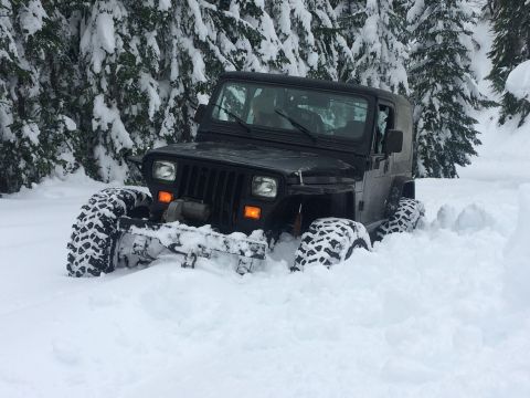 1995 Jeep Wrangler - A black 1995 Jeep Wrangler navigates deep snow during a winter run, with snow-laden trees surrounding the scene.