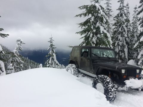 1995 Jeep Wrangler - A Jeep Wrangler navigates a snowy mountain trail, its tires deep in the snow.