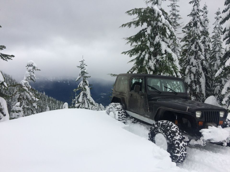 Black Jeep Wrangler with aggressive tires stuck in deep snow on a mountain slope