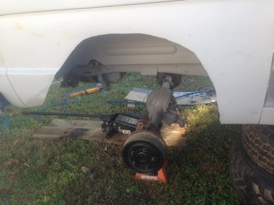 vehicle rear axle removed and supported by a jack and jack stand, with tools on the ground