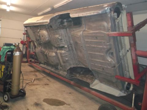 1964 Ford Galaxie - The underside of a car body is suspended on a rotisserie for repair work.
