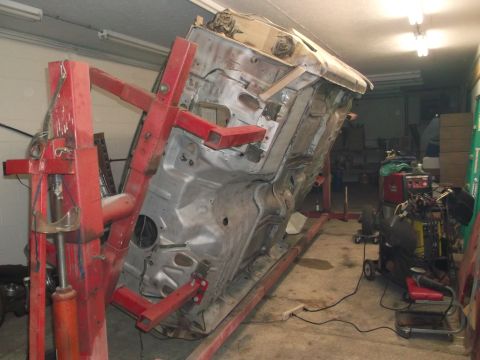 1964 Ford Galaxie - The underside of a 1964 Ford Galaxie body is visible while it's mounted on a red rotisserie lift in a garage.