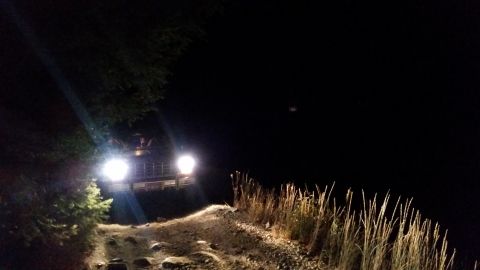 1981 Ford Bronco - A vehicle navigates a rough dirt road at night, illuminated by its headlights.