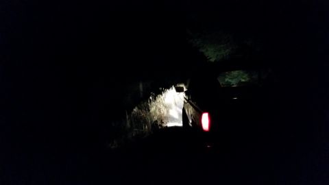 1981 Ford Bronco - A 1981 Ford Bronco navigates a dark, wooded dirt road at night, its taillight glowing red.