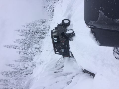 1995 Jeep Wrangler - An off-road vehicle is stuck in deep snow on a steep incline, with another vehicle partially visible.
