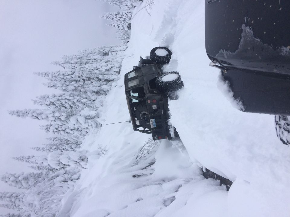 Off-road vehicle tipped over on a snowy slope next to a larger vehicle