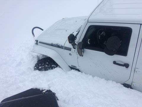 1995 Jeep Wrangler - A white Jeep Wrangler is stuck in deep snow, with only the front fender and tire visible.