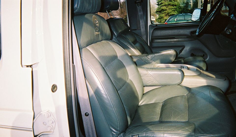 Two-tone gray leather captain's chairs seen through the open passenger door of a white conversion truck