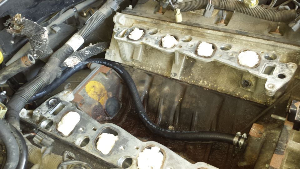 Engine with intake manifold removed, showing cylinder heads and a hose.
