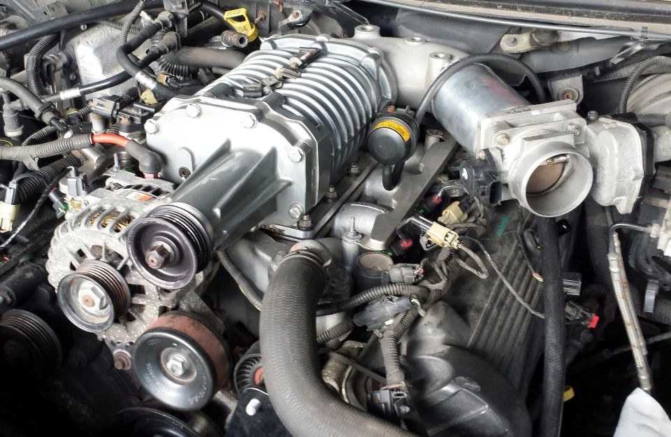 Supercharged V8 engine bay showing roots-type supercharger, alternator, throttle body and belt drive