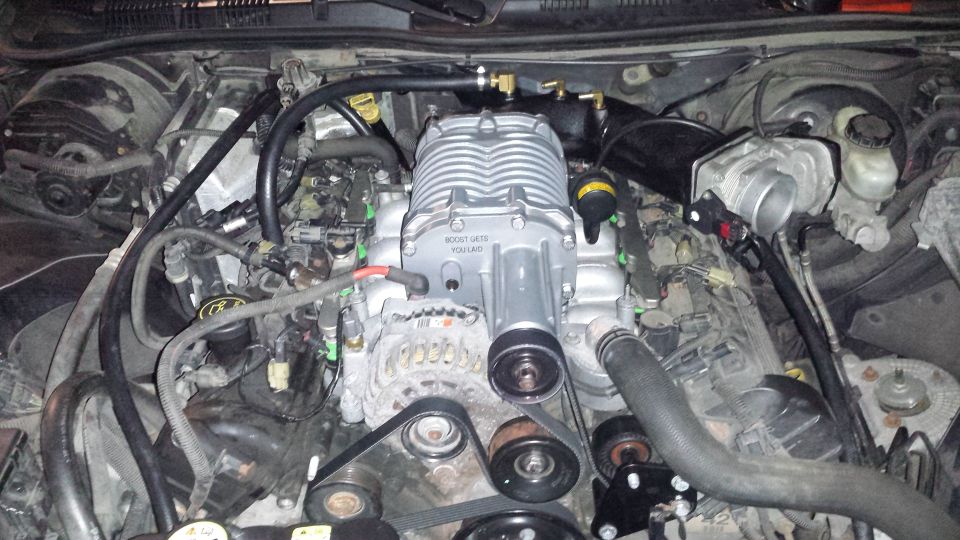 Engine bay with a silver supercharger installed on top of the engine. Text on supercharger reads 'BOOST GATE VQ140'