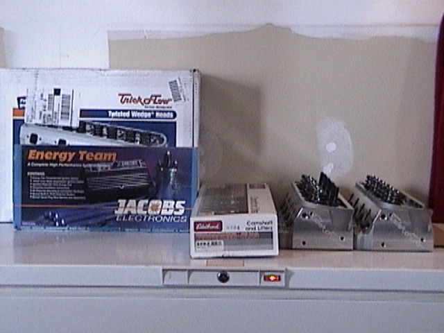 Trick Flow, Jacobs Electronics and Edelbrock parts boxes beside two aluminum cylinder heads on a cabinet