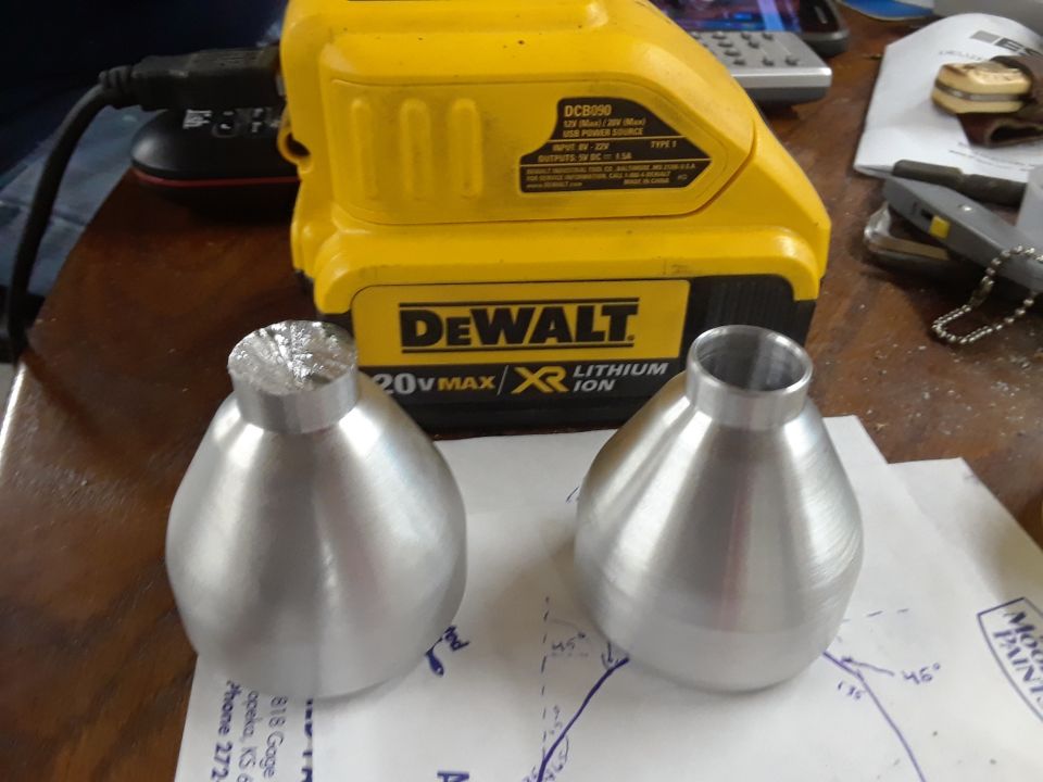 Two custom aluminum parts in front of a DeWalt battery.