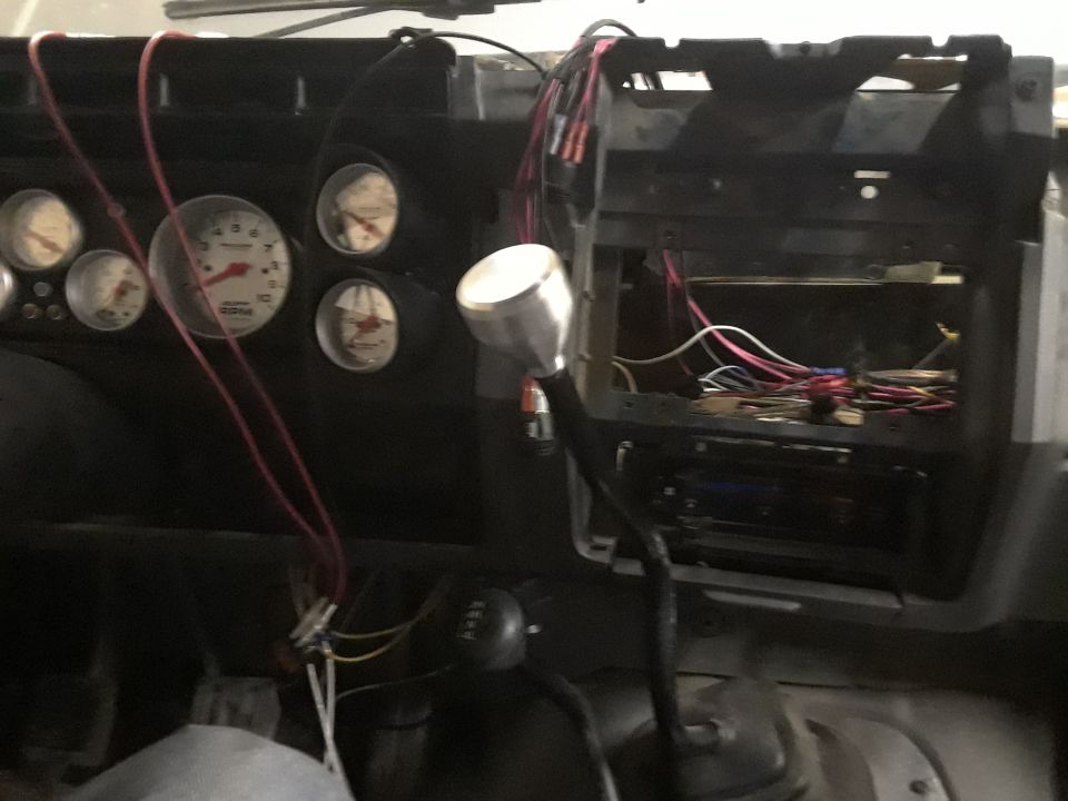 Vehicle interior dashboard with gauges, gear shifter, wiring, and stereo.